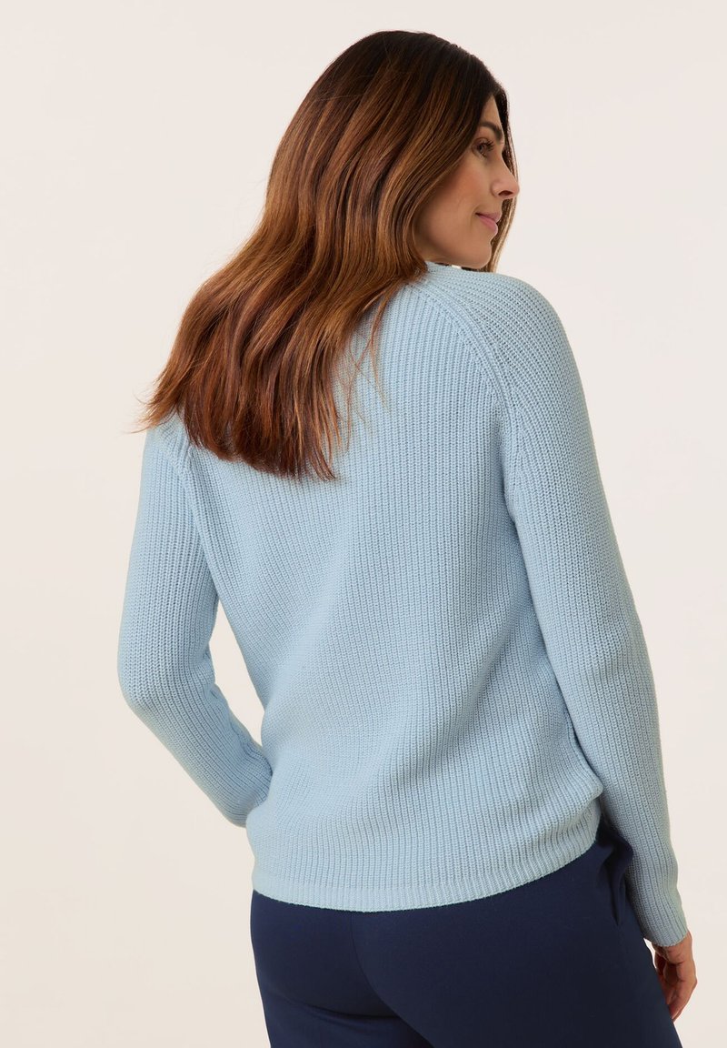 Maglione a costine azzurro chiaro con maniche lunghe, scollatura arrotondata e dettagli di cucitura discreti, indossato con pantaloni blu navy.