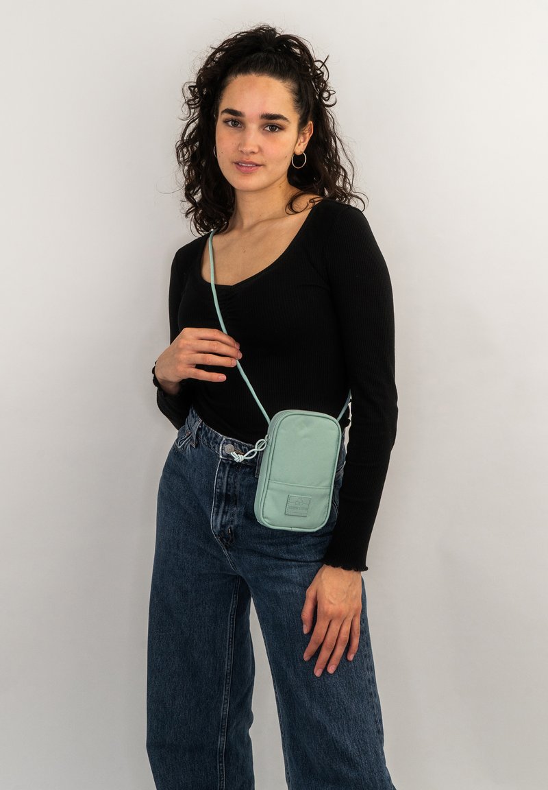 Borsa a tracolla verde menta con una superficie liscia e morbida. Forma rettangolare con una tasca anteriore e tracolla regolabile.