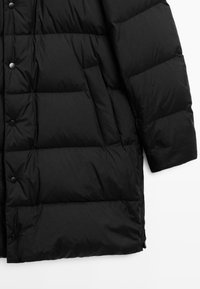 Cappotto puffer imbottito nero con bottoni a scatto, tasca laterale inclinata e maniche lunghe imbottite, mostrato su sfondo bianco.