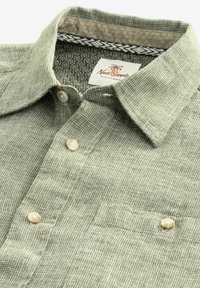 Zielona koszula na guziki w kratę, wykonana z lekkiego materiału, z klasycznym kołnierzykiem i kontrastującą wzorzystą podszewką.