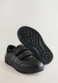 Schwarze Sneakers mit Klettverschlüssen, Obermaterial aus glattem Leder, strukturierte Gummisohle mit Zickzackmuster und Branding an der Seite.