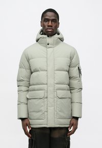 Polstret vinterjakke i lys grå, med høj krave, lynlås lukning, to frontlommer og en aftagelig hætte. Glat tekstur.