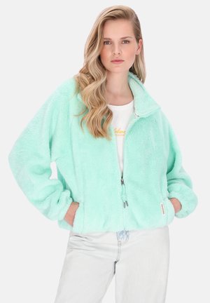 Mentazöld polárdzseki magas gallérral, cipzáros záródással és rugalmas mandzsettákkal. Puha tapintású anyag és laza szabás, világos farmernadrággal párosítva.