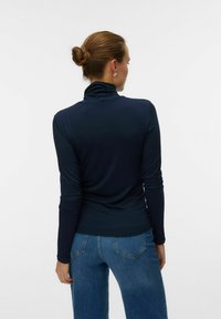 Marineblå turtleneck top lavet af strækbart stof, med lange ærmer og en afslappet pasform, parret med lyseblå bredbenede jeans.