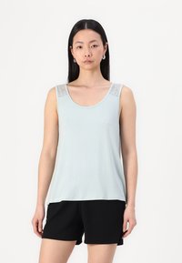 Débardeur bleu clair avec des accents en dentelle sur les épaules. Tissu doux, décolleté arrondi et coupe ample, associé à un short noir.