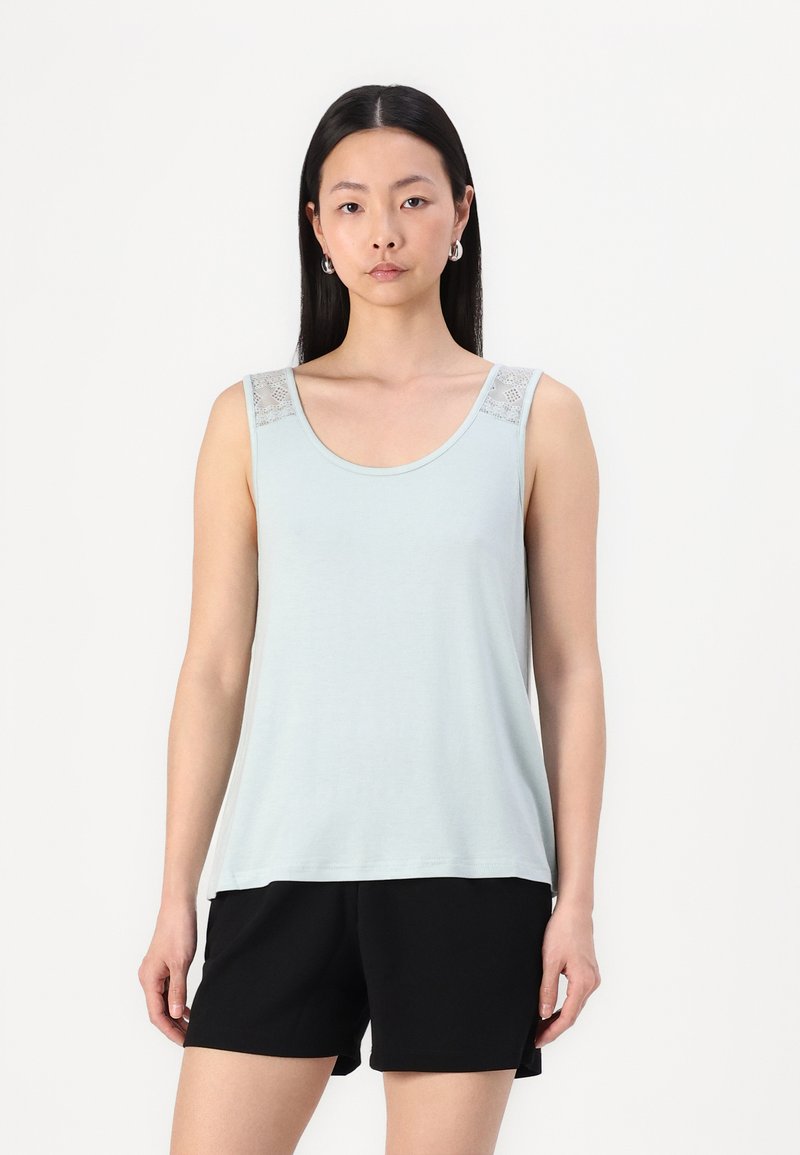 Débardeur bleu clair avec des accents en dentelle sur les épaules. Tissu doux, décolleté arrondi et coupe ample, associé à un short noir.