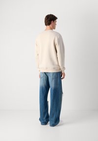 Light beige sweatshirt with a round neckline, dropped shoulders, and ribbed cuffs, paired with oversized, faded blue denim jeans.