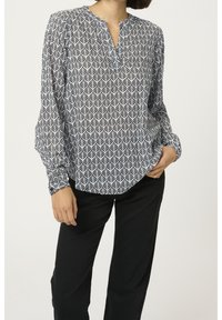 Långärmad blus i vitt och marinblått med ett geometriskt bladmönster, med ståkrage och avslappnad passform. Matchad med svarta byxor.