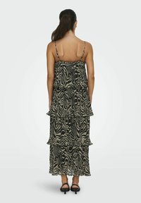 Robe maxi avec un design à volants, présentant un imprimé zèbre abstrait noir et beige, des bretelles fines et une silhouette fluide.