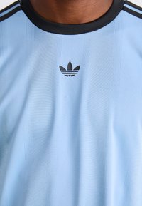Light blue athletic shirt with a black ribbed collar, featuring vertical stripes and a black Adidas logo on the chest.