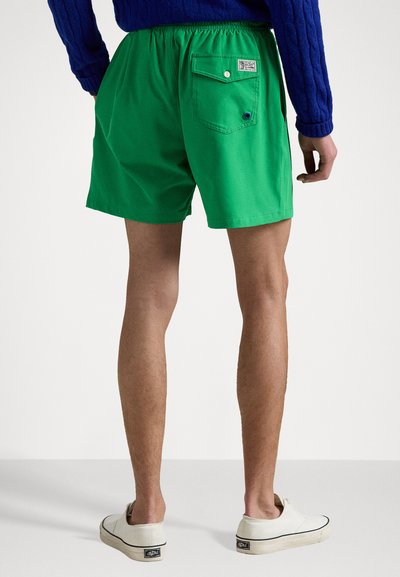 Shorts en coton verts avec une taille élastique, une poche arrière et un détail en bouton. Associés à des chaussures légères à enfiler.