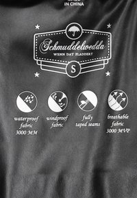 Fekete vízálló anyag fehér szöveggel. Fő jellemzők: vízálló (3000 MM), szélálló, teljesen varrt varrásokkal és légáteresztő (3000 MVP).