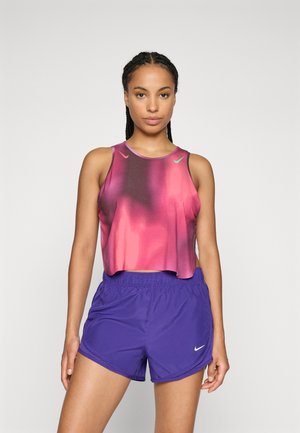 Vijolične športne kratke hlače v kombinaciji z raztegnjeno majico brez rokavov, ki vsebuje gradientni vzorec v roza in temno vijolični barvi. Obe oblačili imata logotipa Nike.