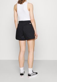 Černé šortky s elastickým pasem a zadní kapsou, spárované s bílým tílkem a černo-bílými kostkovanými slip-on обувí.