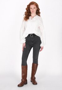 Weiße Spitzenbluse mit gerafftem Ausschnitt und schmalen Ärmeln; kombiniert mit grauen Skinny-Jeans und braunen kniehohen Lederstiefeln.