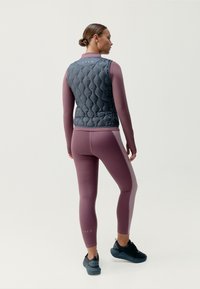Puchowy szary kamizelka w diamentowy wzór, połączona z dopasowanymi bordowymi legginsami. Oba elementy charakteryzują się elegancką, gładką teksturą; czarne buty sportowe dopełniają całości.