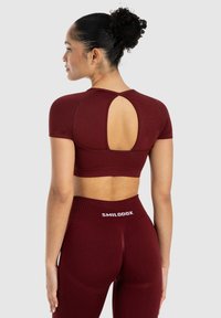 Bordeaux sport crop top med korte ærmer, med en udskæring på ryggen. Sammen med matchende højtaljede leggings. Glat tekstur.