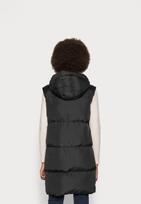 Gilet imbottito nero con cappuccio, caratterizzato da un design trapuntato e cuciture verticali. Il gilet è lungo fino al ginocchio e presenta una texture liscia e lucida.