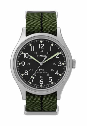 Hodinky Timex MK1 s čiernym ciferníkom, bielymi číslicami, zelenými luminiscenčnými ručičkami, strieborným puzdrom a zeleným látkovým remienkom s čiernym prúžkom.