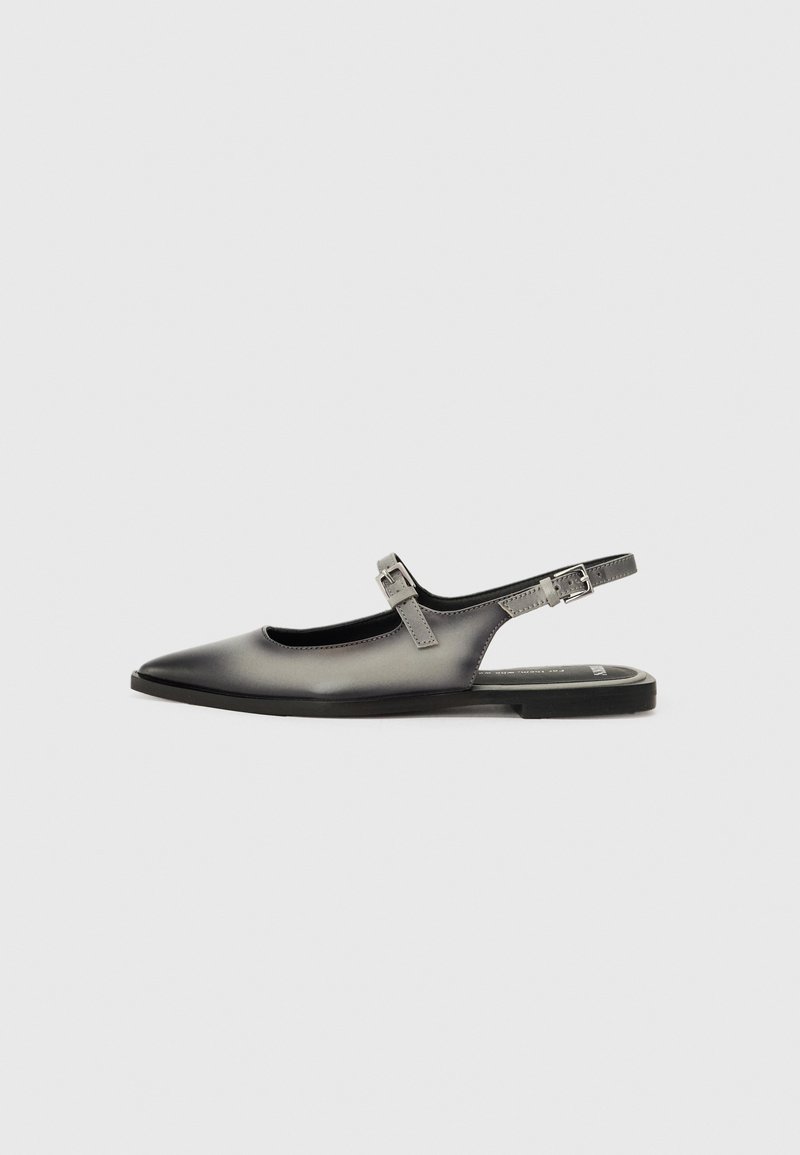 Chaussure slingback plate en cuir noir avec deux brides réglables à boucle et bout pointu sur fond blanc.