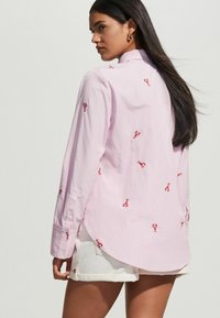 Light pink long-sleeve shirt with red lobster embroidery, featuring a striped pattern, button cuffs, and a curved hemline.
