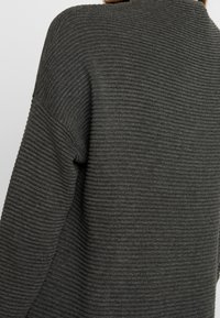 Pull gris foncé avec une texture côtelée, présentant une coupe décontractée et des coutures d'épaules larges et tombantes. Design minimaliste, sans accents visibles.