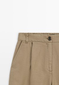 Beige Leinenmischhosen mit Knopfverschluss, Bügelfalten und Seitentaschen. Weiche Textur mit glattem Finish.