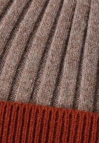 Sezione di maglione lavorato a maglia con texture a coste marroni, caratterizzata da schemi alternati di larghe e strette coste, rifinita con un orlo a coste di colore ruggine.