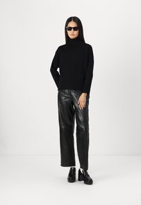 Svart turtleneck genser med lange ermer, parret med glitrende, løstsittende svarte skinnbukser. Brukt med svarte solbriller og kraftige plattformsko.