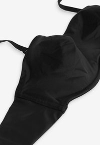 Schwarzer gepolsterter BH mit verstellbaren Trägern, flach auf einer weißen Oberfläche liegend, zeigt die Form der Cups und die Nahtdetails.