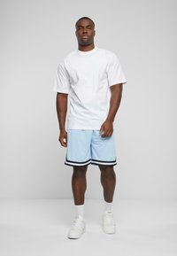 Hvid kortærmet t-shirt parret med lyseblå træningsshorts med sorte striber. Modellen bærer hvide sneakers og ankelsokker.