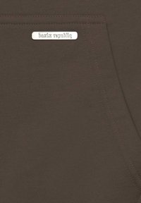 Smeđi materijal glatke teksture, s srebrnom etiketom na kojoj piše "bazir republic" i detaljem ušivenog džepa.
