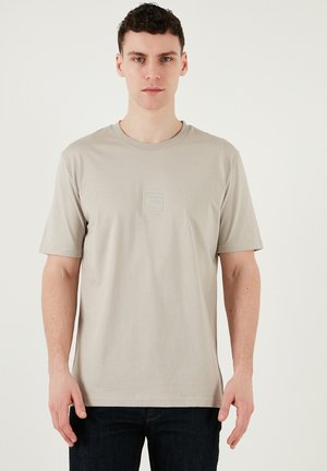 Šviesiai kreminės spalvos T-shirt, pagamintas iš švelnaus medvilnės, su apvalia iškirpte, trumpomis rankovėmis, su subtiliu iškilniu logotipu ant krūtinės ir klasikinio kirpimo.