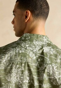 Krátky rukáv zelená košeľa so bielymi botanickými a krajinnými ilustráciami, dvojitými gombíkmi na zadnej strane a uvoľneným strihom.