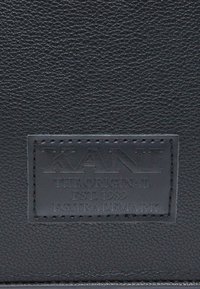 Crni teksturirani kožni uložak s utisnutim logotipom "KANI", uz tekst "THE ORIGINAL EST. 1989 E.G. TRADEMARK" u pravokutnom formatu.