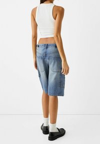 Denim cargo shorts i ljusblått, med flera fickor och en avslappnad passform. Kombinerat med en vit ärmlös topp och svarta skor.