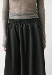 Pantaloni neri a gamba ampia con vita elasticizzata. Il tessuto è liscio e leggermente lucido. Abbinati a un top aderente in maglia grigia.