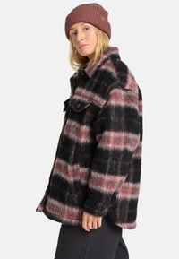 Geruite wollen jas in zwart, roze en wit met een relaxte pasvorm, knoopsluiting en twee borstzakken; gecombineerd met een geribde bruine beanie.