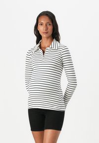 Vit långärmad polo med marinblå horisontella ränder, ribbad textur och krage. Kombinerad med svarta figursydda shorts.