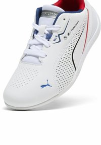 Baskets de sport blanches en cuir synthétique, avec des motifs perforés, des accents bleus et rouges, des lacets et le logo Puma sur le côté.