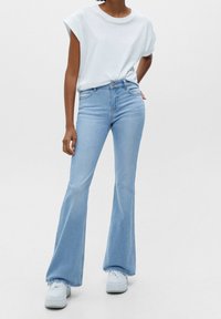Jean évasé bleu clair à taille haute, associé à un t-shirt blanc en coton simple. Le jean présente un design épuré et un minimum de détails.