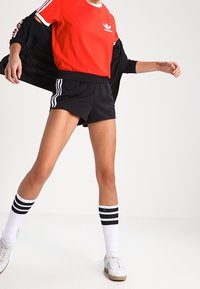 Czerwona koszulka Adidas z krótkim rękawem i białym kołnierzykiem, w połączeniu z czarnymi szortami sportowymi. Białe skarpetki w czarne paski i jasne buty.