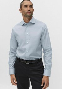 Lyseblå ternet skjorte med lange ærmer, knapkrave og matchende knapper. Bæres med sorte bukser og et sort bælte.