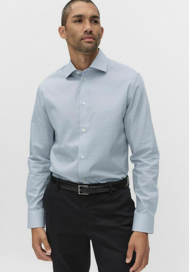 Lyseblå ternet skjorte med lange ærmer, knapkrave og matchende knapper. Bæres med sorte bukser og et sort bælte.