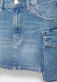 Jeanskjol i ljusblått, med hög midja, fickor och kontrasterande sömmar. Nederkanten är rå och något slitna för en avslappnad look.