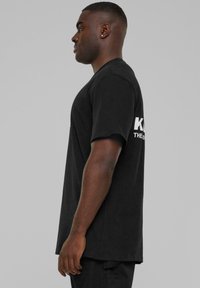 Black short-sleeve t-shirt made of cotton, featuring a crew neck and white text on the sleeve. Simple design with a relaxed fit.