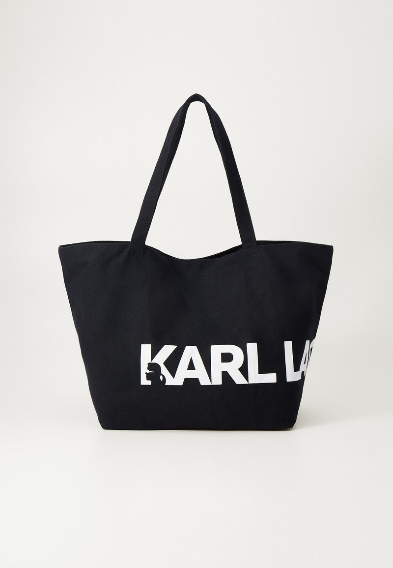 Sac fourre-tout noir en tissu durable avec deux longues poignées. Présente un grand texte blanc "KARL LAGERFELD" et un logo en silhouette sur le devant.
