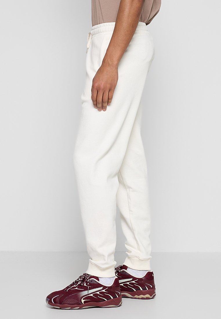 Pantalones de chándal blancos de algodón con cintura elástica y cordón, con puños en los tobillos y un corte holgado, combinados con zapatillas burdeos.