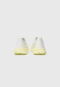 Baskets de sport blanches avec des accents jaunes, présentant un dessus texturé, un bout rond et une semelle rembourrée. Logo sur le talon.