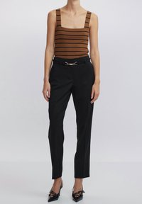 Top tipo tank de rayas marrones con tirantes anchos, combinado con pantalones negros de corte entallado y zapatos de tacón negros con un acento de lazo.